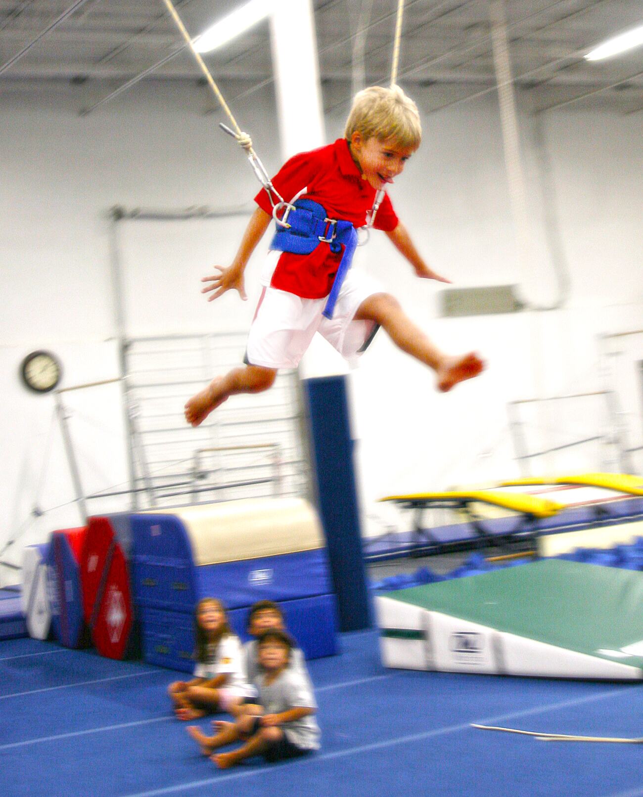 A young gymnast on the bungee harness while classmates watch