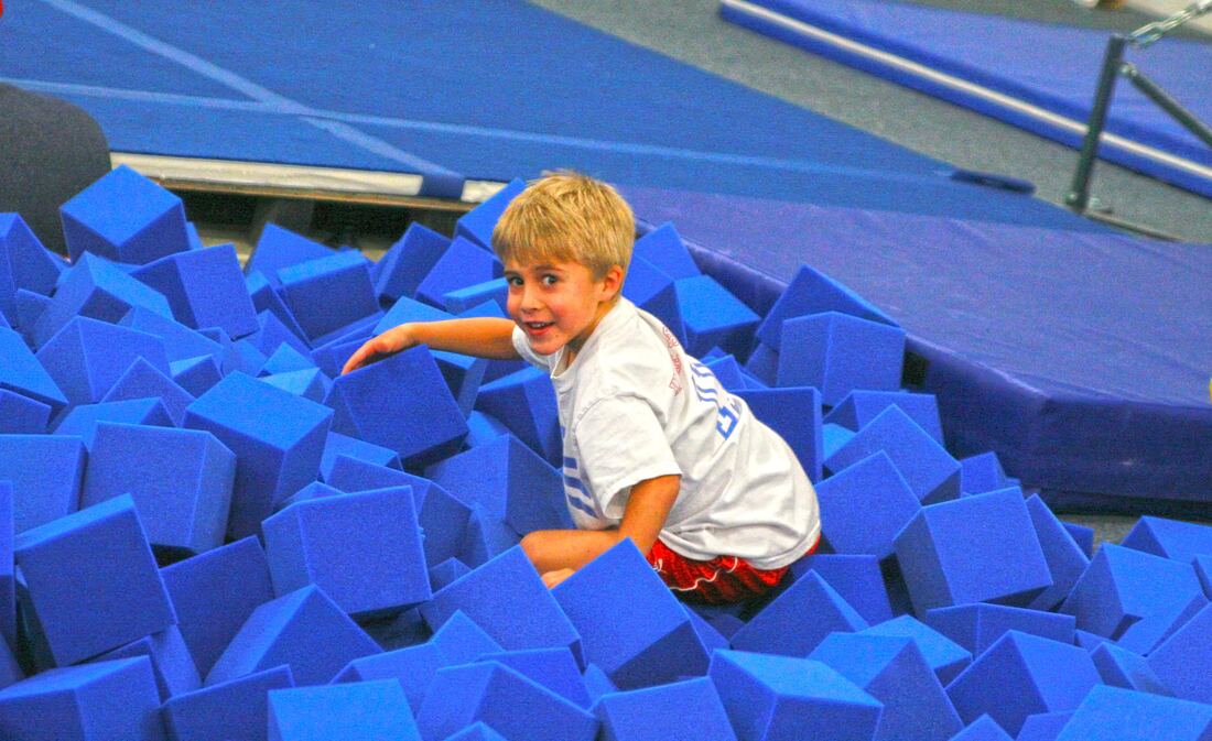 A young gymnast playing in the blue foam pit