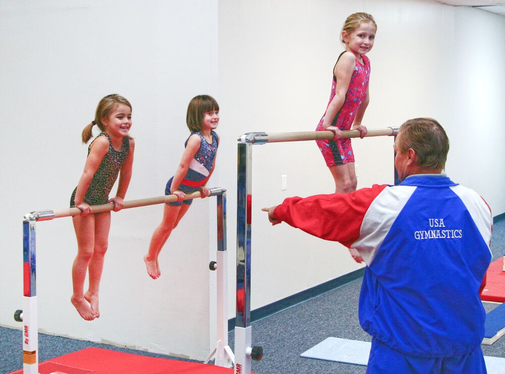 A young gymnast on the bar with a coach spotting